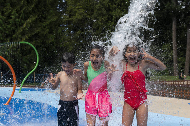 Kids standing under a Waterplay Sling Soaker during the grand opening of the new Generations Playground Splash Pad in White Rock, BC