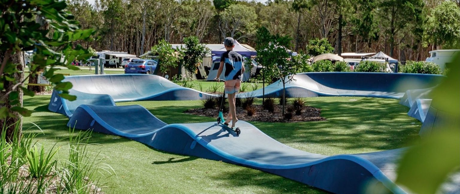 Kid using a scooter on a Parkitect pump track in a community park