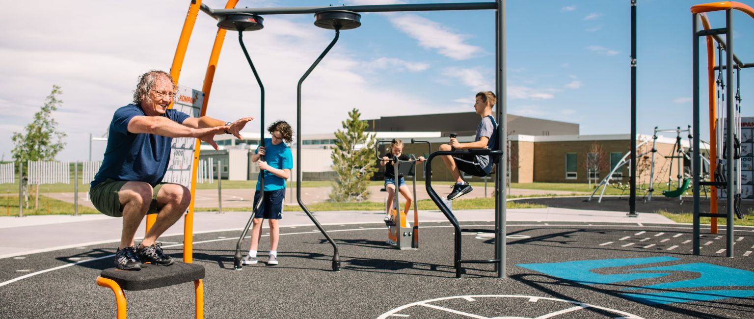 A family of all ages utilizes the outdoor fitness equipment at Watermark Park in Lethbridge, AB