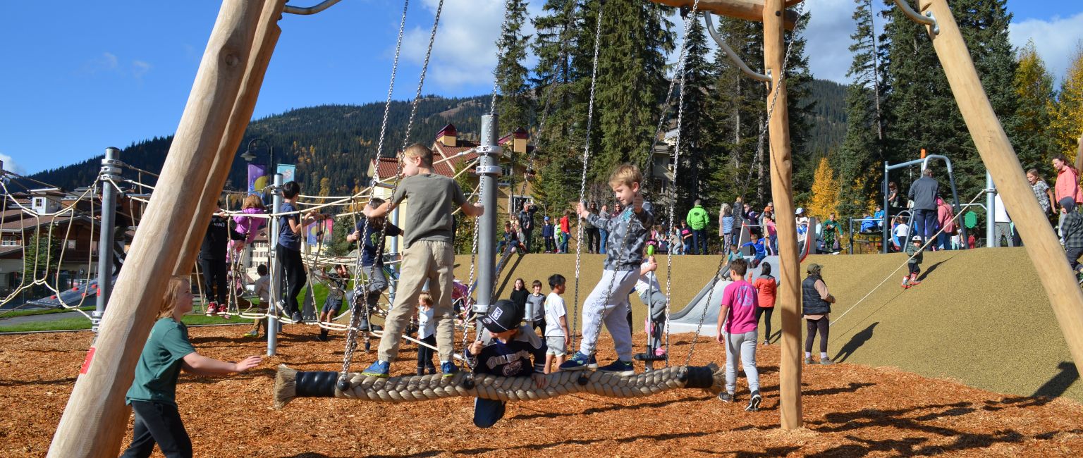 Kids collaboratively playing on a piece of playground equipment at a busy park