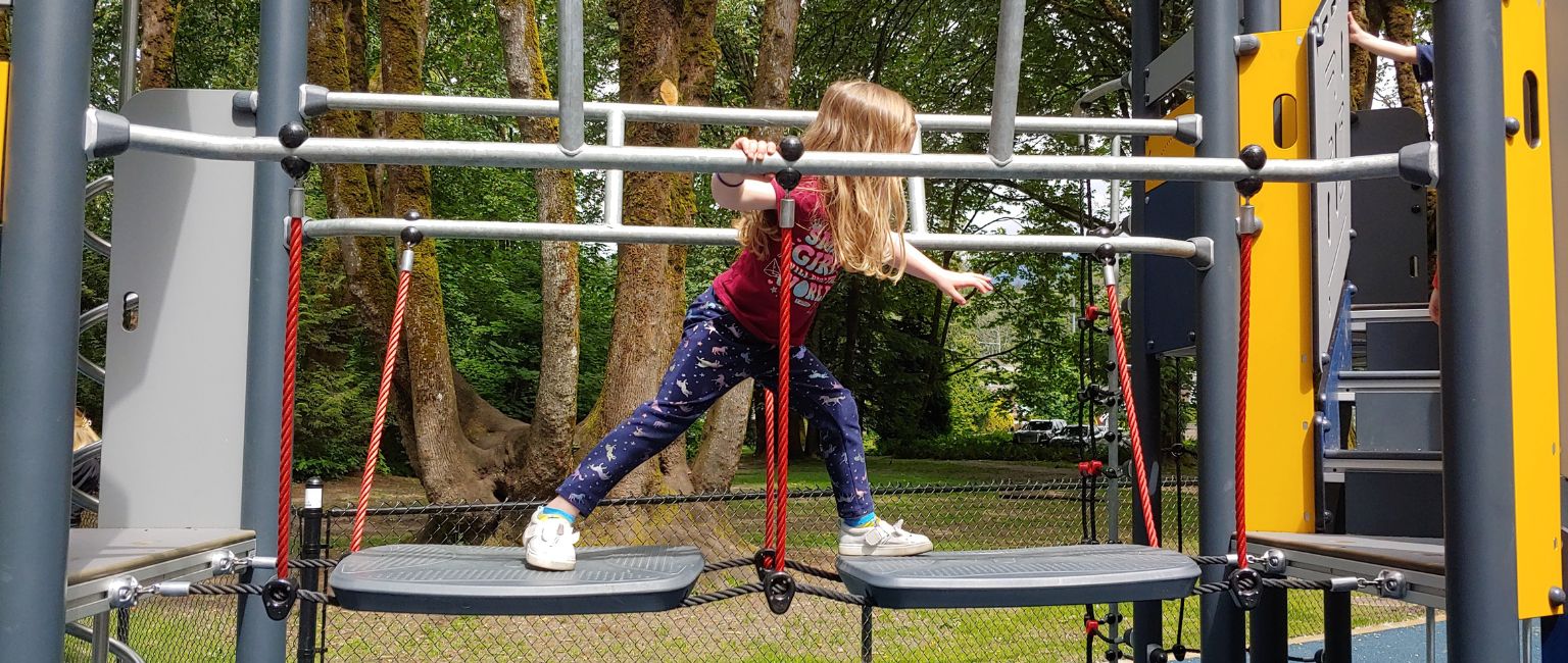 Young girl carefully moving across a wobble bridge on a playground climbing structure