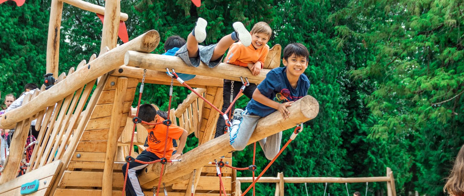A group of young boys play on the end of a play structure shaped like a pirate ship.