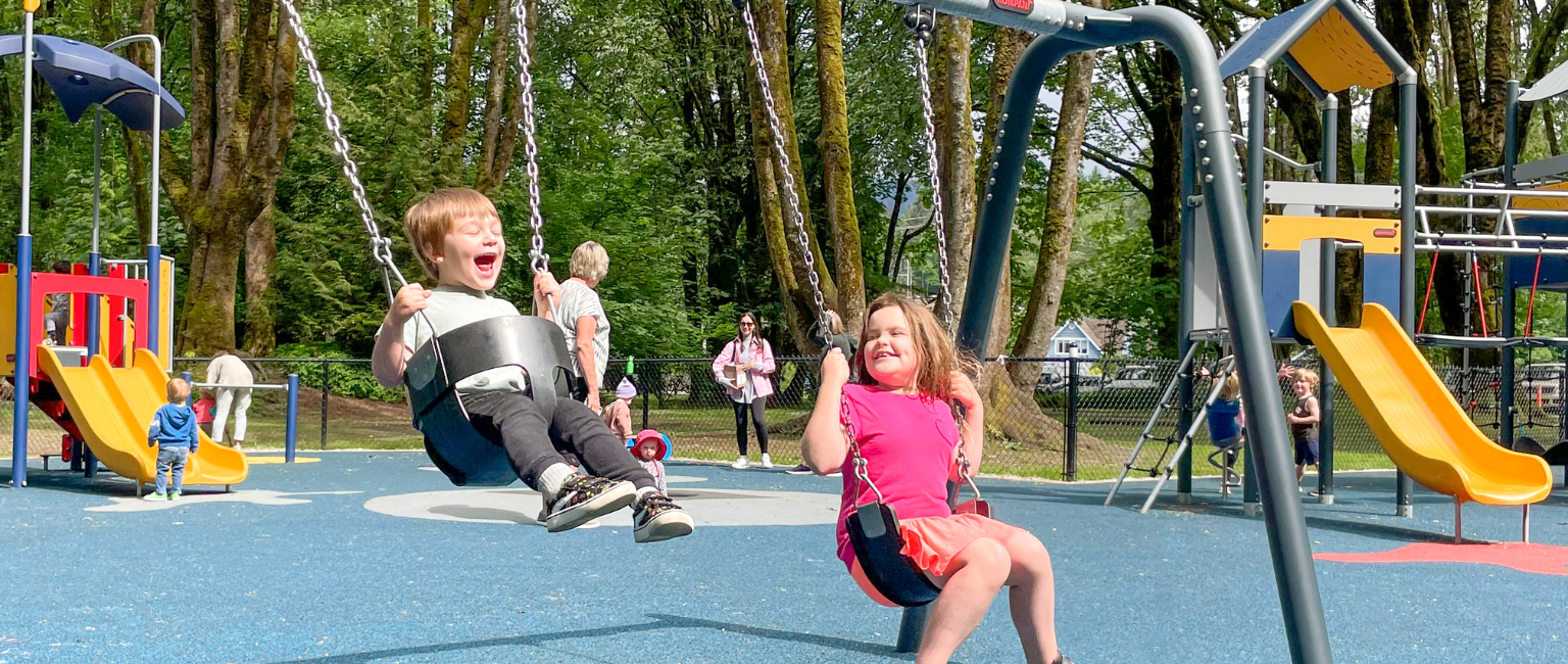 Young boy and girl swinging on swingset in community playground, laughing and having a good time