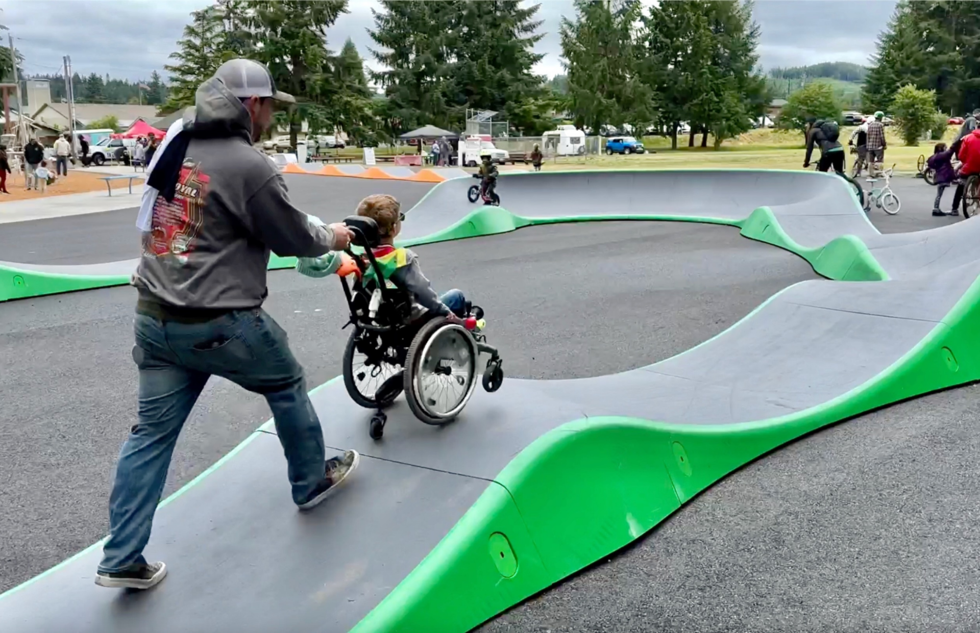 Parent pushing a kid in a wheelchair on a Parkitect Park pump track
