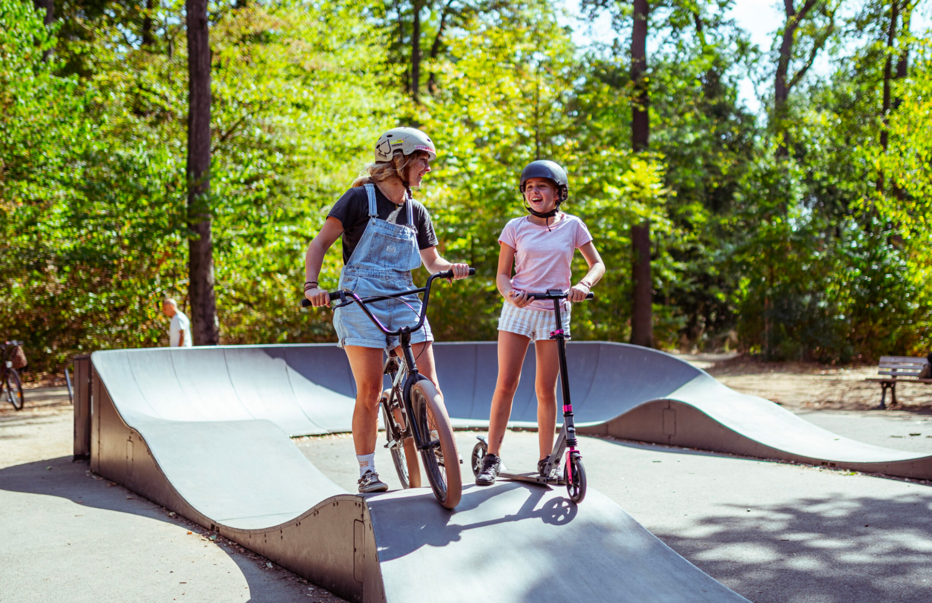 Two girls riding scooters on a Parkitect Premium pump track