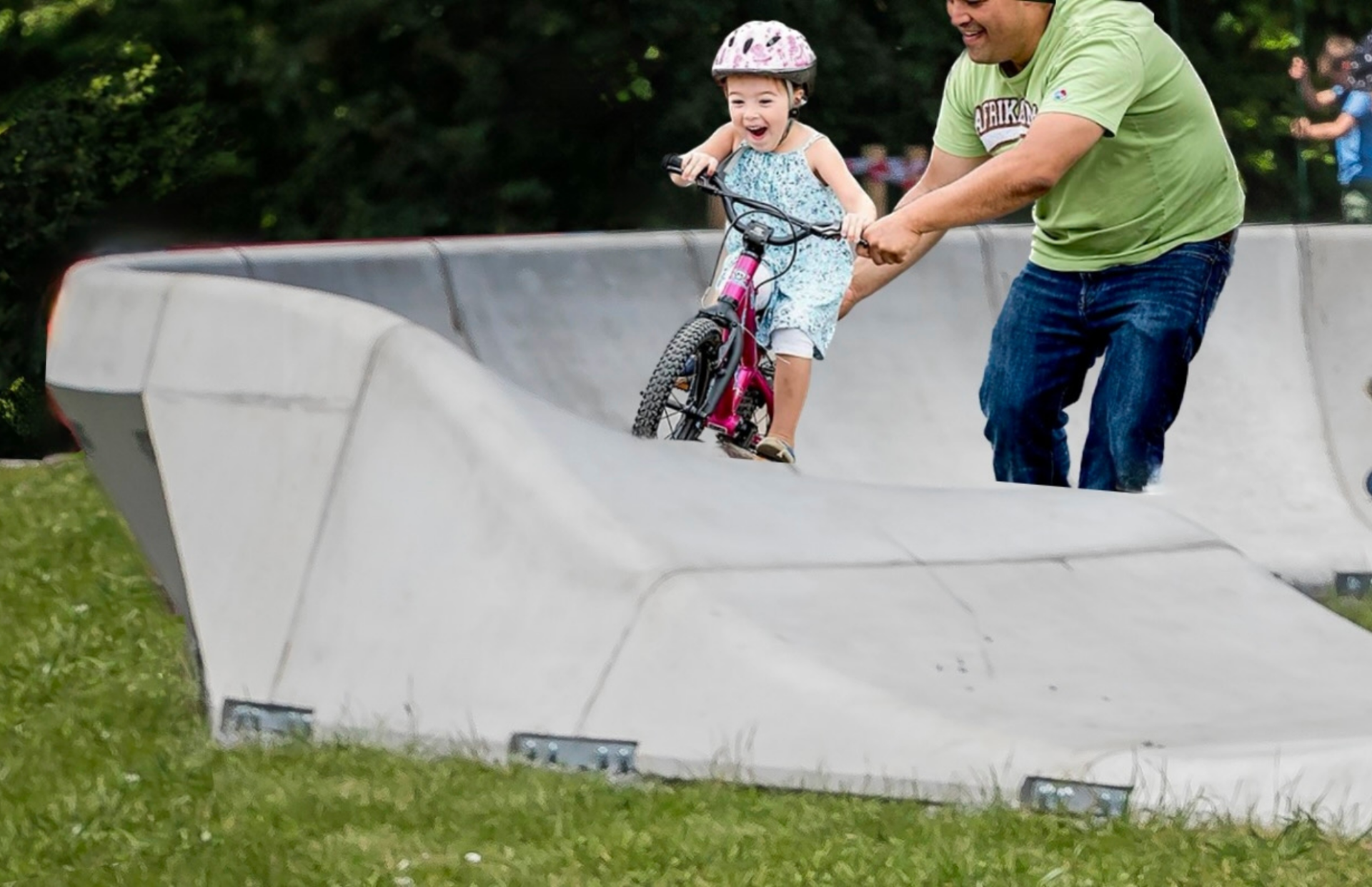 Parent pushing young girl on a bike on a Parkitect Urban pump track