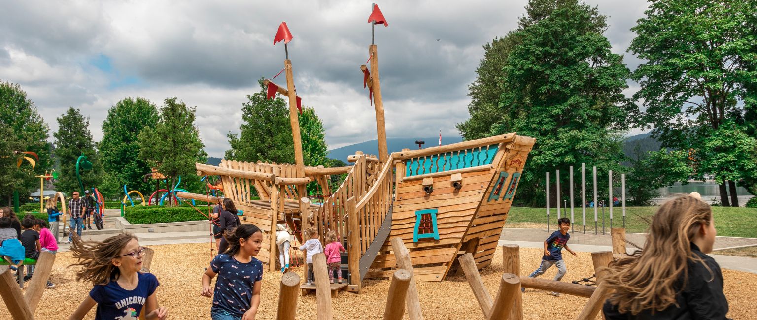 Pirate ship play structure in a community playground with excited kids running around it.