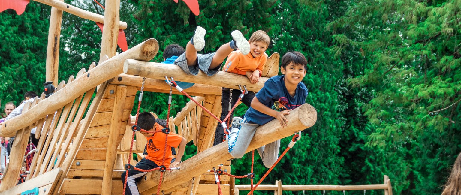 Young kids climbing and playing on the back of a KOMPAN ship play structure in a community playground